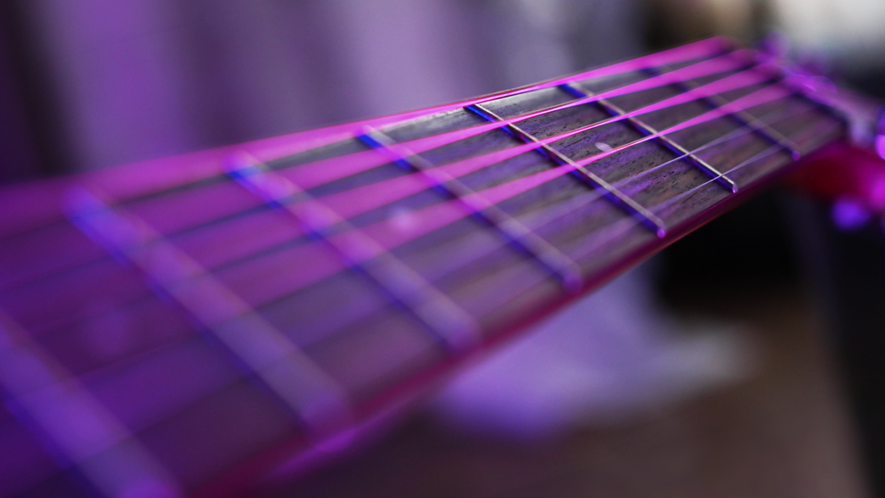 Corde per chitarra acustica in primo piano sulla tastiera, illuminate di viola